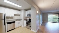 Located at 18 Griffin Terrace in Weymouth, MA, this single-floor unit offers a thoughtfully arranged layout with a clean, contemporary aesthetic throughout. Neutral gray walls and white trim create a cohesive, modern palette that flows from room to room.

The kitchen is a functional highlight, equipped with a full suite of stainless steel appliances including a refrigerator, electric range, built-in microwave, and dishwasher. White cabinetry provides ample storage, while light hardwood-style flooring and recessed fluorescent lighting keep the space bright and practical. The kitchen opens toward a hallway that connects to the main living areas seamlessly.

The living area is generously proportioned, featuring the same light hardwood-style flooring and a sliding glass door that opens to a private balcony overlooking greenery, filling the room with natural light and outdoor views. A wall-mounted air conditioning unit ensures year-round comfort.

The bedroom is carpeted for warmth and comfort, featuring a large window with leafy views, baseboard heating, and access to a walk-in closet with built-in shelving for organized storage.

The bathroom is clean and straightforward, with a full tub and shower combination, wood-style flooring, and brushed nickel fixtures and towel bars throughout.