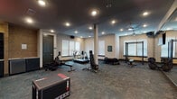 Located at 2161 Nolensville Pike in Nashville, Tennessee, this well-equipped fitness center offers a comprehensive workout environment designed to support a wide range of exercise routines. The single-floor facility features a spacious, open layout with durable slate-toned flooring throughout, dark ceiling accents, and recessed lighting complemented by ceiling fans that ensure consistent airflow and comfort during workouts.

The main workout area is furnished with cardio equipment including treadmills, an elliptical, and a rowing machine, alongside adjustable weight benches and a cable machine for strength training. A large wall-mounted mirror spans one section of the space, enhancing the sense of openness and allowing users to monitor their form. Natural light filters in through multiple windows fitted with white blinds, brightening the neutral-toned walls.

A dedicated functional training zone houses an organized equipment rack stocked with kettlebells, medicine balls, stability balls, resistance bands, and a heavy punching bag — ideal for high-intensity and cross-training workouts. A plyo box sits prominently in this area, supporting explosive training exercises. Additional storage cabinetry and a textured accent wall add a refined, purposeful aesthetic. The overall ambiance is modern and focused, providing a motivating environment for users of all fitness levels.