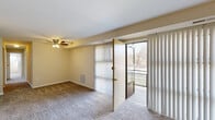 This single-floor residence offers a practical and efficient layout across three bedrooms, two bathrooms, and a combined living and dining area. The kitchen features dark espresso cabinetry extending to the upper walls, light countertops, wood-look vinyl flooring, and a full suite of white appliances including a refrigerator, electric range, and sink — all illuminated by a flush overhead fluorescent light. The open living and dining area is carpeted and filled with natural light, with a ceiling fan overhead and sliding glass doors that open to an outdoor balcony, offering views of surrounding greenery. Each of the three bedrooms is carpeted and features wide windows that allow natural light and outdoor views, with at least two of the bedrooms equipped with dedicated closets offering shelving for organized storage. The primary bedroom includes a ceiling fan and its own closet. Both bathrooms are finished with subway tile wainscoting, vanity mirrors with lighted fixtures, and clean white fixtures throughout — one featuring a shower/tub combination. Five closets distributed throughout the unit provide generous storage capacity, complemented by a hallway that connects the rooms in a logical flow.