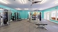 Located at 3301 Cotton Mill Dr in Raleigh, NC, this fitness center is a comprehensive, single-floor facility designed to support a wide range of workout routines. The space is organized into distinct zones, each thoughtfully appointed with specific equipment and a vibrant color palette of teal and chartreuse green that creates an energizing atmosphere throughout.

The main strength training area features a power rack, a cable machine system, a full dumbbell rack, a kettlebell station with a variety of weights, medicine balls, an adjustable bench, and a heavy bag — offering everything needed for a complete resistance and functional training session. Large mirrors line the walls, and ceiling fans keep air circulating overhead.

A dedicated cardio zone, accented with bright yellow-green walls, houses multiple Matrix treadmills, elliptical trainers, a stair climber, and a recumbent bike. Generous windows flood this area with natural light and provide views of the surrounding greenery and an outdoor pool area, accessible through a set of French doors.

A separate cycling studio features Matrix spin bikes, stability balls, step platforms, and a wall-mounted display screen, set beneath crown molding and a tray ceiling with a ceiling fan — lending a polished, boutique-studio feel. Striped carpet tile flooring unifies the main areas, while the cycling room features a smooth, easy-clean floor surface.