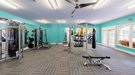 Located at 3301 Cotton Mill Dr in Raleigh, NC, this fitness center is a comprehensive, single-floor facility designed to support a wide range of workout routines. The space is organized into distinct zones, each thoughtfully appointed with specific equipment and a vibrant color palette of teal and chartreuse green that creates an energizing atmosphere throughout.

The main strength training area features a power rack, a cable machine system, a full dumbbell rack, a kettlebell station with a variety of weights, medicine balls, an adjustable bench, and a heavy bag — offering everything needed for a complete resistance and functional training session. Large mirrors line the walls, and ceiling fans keep air circulating overhead.

A dedicated cardio zone, accented with bright yellow-green walls, houses multiple Matrix treadmills, elliptical trainers, a stair climber, and a recumbent bike. Generous windows flood this area with natural light and provide views of the surrounding greenery and an outdoor pool area, accessible through a set of French doors.

A separate cycling studio features Matrix spin bikes, stability balls, step platforms, and a wall-mounted display screen, set beneath crown molding and a tray ceiling with a ceiling fan — lending a polished, boutique-studio feel. Striped carpet tile flooring unifies the main areas, while the cycling room features a smooth, easy-clean floor surface.