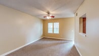 This single-floor unit offers a functional and well-organized layout across two bedrooms and two bathrooms. The living area is generously proportioned, finished with neutral-toned carpet and warm beige walls. A ceiling fan with a built-in light fixture provides both comfort and illumination, while a window allows natural light to fill the space. A pass-through opening connects the living area directly to the kitchen, enhancing the sense of openness between the two spaces.

The galley-style kitchen features warm wood cabinetry lining both sides, granite-style countertops, a double sink, and white appliances including a coil-burner range and refrigerator. Light flooring runs throughout, contributing to a bright and clean appearance.

Both bedrooms are carpeted and share a similar aesthetic, with neutral walls, windows admitting natural light, and ceiling-mounted light fixtures. Each room offers a comfortable footprint suitable for standard furnishings.

The two bathrooms are consistent in design, each featuring wood cabinetry, granite-style vanity countertops, and tile flooring. One bathroom includes a shower-tub combination, while the other is configured as a more compact layout. Textured ceilings are present throughout the unit, adding a consistent design element across all rooms.