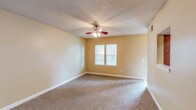 This single-floor unit offers a functional and well-organized layout across two bedrooms and two bathrooms. The living area is generously proportioned, finished with neutral-toned carpet and warm beige walls. A ceiling fan with a built-in light fixture provides both comfort and illumination, while a window allows natural light to fill the space. A pass-through opening connects the living area directly to the kitchen, enhancing the sense of openness between the two spaces.

The galley-style kitchen features warm wood cabinetry lining both sides, granite-style countertops, a double sink, and white appliances including a coil-burner range and refrigerator. Light flooring runs throughout, contributing to a bright and clean appearance.

Both bedrooms are carpeted and share a similar aesthetic, with neutral walls, windows admitting natural light, and ceiling-mounted light fixtures. Each room offers a comfortable footprint suitable for standard furnishings.

The two bathrooms are consistent in design, each featuring wood cabinetry, granite-style vanity countertops, and tile flooring. One bathroom includes a shower-tub combination, while the other is configured as a more compact layout. Textured ceilings are present throughout the unit, adding a consistent design element across all rooms.