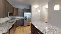 Located at 1743 Central Park Road in Charleston, South Carolina, this single-floor residence offers a well-designed layout that balances comfort and functionality. The kitchen serves as a central highlight, featuring rich dark cabinetry, granite countertops, a granite-topped island with pendant lighting, and a full suite of stainless steel appliances including a refrigerator with ice maker, electric range, microwave, and dishwasher. Light wood-style flooring runs throughout the kitchen and connecting living areas, contributing to a clean, modern aesthetic. The living area is bright and airy, benefiting from multiple windows with slatted blinds that invite natural light and provide views of the surrounding greenery. A ceiling fan overhead adds to the comfort of the space, and a door opens to an outdoor balcony area. The bedroom is finished with plush carpeting and features dual windows with natural light, along with its own ceiling fan. The bathroom is thoughtfully appointed with a granite-top vanity, wood-toned cabinetry, a full tub-shower combination, and light wood-style flooring. A dedicated laundry room provides added convenience, equipped with a full-size front-loading washer and dryer alongside built-in wire shelving for storage. The overall palette of soft neutrals and quality finishes gives this residence a polished, move-in-ready character.