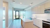 Located at 9 Harrington Street in the heart of downtown Raleigh, NC, this modern high-rise unit offers a sleek, contemporary living experience with thoughtfully designed spaces and high-end finishes throughout. The open-concept layout seamlessly connects the kitchen and living areas, maximizing the sense of space and flow.

The kitchen is a standout feature, equipped with light wood flat-front cabinetry extending to the ceiling, white quartz countertops, a subway tile backsplash, stainless steel appliances including a refrigerator with ice maker, electric range, microwave, and dishwasher, as well as a central island that provides additional prep and seating space.

The living and bedroom areas are bathed in abundant natural light, courtesy of expansive floor-to-ceiling windows and sliding glass doors that open to a private balcony offering sweeping panoramic views of the Raleigh skyline and surrounding greenery. Light wood-tone flooring runs consistently throughout the unit, complementing the neutral wall tones and clean architectural lines.

The bathroom includes a soaking tub with tiled surround, a white vanity with an undermount sink, and modern fixtures. Additional highlights include a walk-in closet with built-in shelving systems, an in-unit stacked washer and dryer, and recessed lighting throughout.