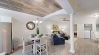 Located at 1184 Waxwing Dr in Florence, SC, this two-story home offers four bedrooms and three bathrooms across two thoughtfully designed floors. The main level serves as the heart of the home, where an open-concept living and dining area immediately impresses with its striking wood-plank ceiling, decorative arched entryway, and a classic white column that elegantly divides the spaces. Light wood-tone flooring flows throughout, complementing the bright, neutral palette. The dining area is anchored by a chandelier, while the adjacent living room features a ceiling fan and generous natural light. The galley-style kitchen is outfitted with white shaker cabinetry, subway tile backsplash, light stone countertops, stainless steel appliances, and a wood-plank ceiling detail that ties seamlessly to the main living areas. One bedroom on the main floor doubles as a flexible office space and includes convenient access to an in-unit washer and dryer. The bathrooms feature granite vanity tops and wood-framed mirrors. Upstairs, the spacious primary suite is a standout, boasting a tray ceiling with crown molding detail and two walk-in closets. Additional bedrooms are bright and comfortable, each with ceiling fans and natural light from well-placed windows. This home combines refined architectural details with practical, modern living.