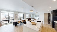 This contemporary two-story residence offers a thoughtfully designed layout across two floors, with the main level comprising the majority of the living space. The open-concept main floor seamlessly connects the kitchen, dining area, and living room, creating an expansive and light-filled environment. Large floor-to-ceiling windows and sliding glass doors frame sweeping urban skyline views, flooding the interior with natural light throughout the day.

The kitchen is a standout feature, anchored by a generous waterfall quartz island with bar seating, two-tone cabinetry in white and dark finishes, a white tile backsplash, and stainless steel appliances. Pendant lighting adds a refined touch overhead. The adjacent dining area comfortably accommodates a full dining table and benefits from the same panoramic city views.

The primary bedroom is generously proportioned, featuring light hardwood flooring, a clean white palette, and direct access to a private balcony with outdoor views. A walk-in closet with built-in shelving and hanging rods provides ample storage. The bathrooms are elegantly finished, with one showcasing a glass-enclosed walk-in shower clad in large-format marble-style tile. A dedicated laundry room with full-size washer and dryer adds everyday convenience. Two staircases connect the floors, enhancing accessibility throughout the home.