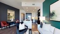 This thoughtfully designed single-floor residence showcases a contemporary aesthetic characterized by bold accent walls, rich hardwood flooring, and a cohesive color palette of deep teals, charcoal, and crisp white throughout.

The open-concept living, dining, and kitchen area serves as the social core of the home. The living room features a striking teal accent wall, floor-to-ceiling windows offering outdoor views, and access to a balcony. A floating media console anchors the space opposite a dedicated dining area with a dark accent wall and mirror detail.

The kitchen is outfitted with stainless steel appliances including a gas range, French door refrigerator, built-in wine cooler, and a stainless hood. Contrasting dark lower cabinetry and white upper cabinets flank a waterfall-edge island with a marble-look countertop.

The primary bedroom features a teal accent wall, plush carpet, natural light, and a spacious walk-in closet with built-in dark wood organizers. A secondary room functions as a flexible office or den with shelving and large windows.

A powder room with deep plum walls and pedestal sink adds character, while a dedicated laundry closet with stacked washer and dryer provides practical convenience.