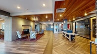 Located at 133 Summit St in Duluth, MN, this single-floor community space offers a generous and well-appointed interior designed with both comfort and functionality in mind. The space immediately impresses with its striking herringbone-patterned hardwood flooring, rich wood-paneled ceilings, and a cohesive contemporary design language carried throughout.

The main lobby and lounge area serves as the heart of the space, featuring a sleek built-in fireplace framed in stone-textured surround, a wall-mounted TV, and comfortable seating arranged on vibrant area rugs. A prominent reception desk with a two-tone white and navy finish anchors the entry zone, complemented by pendant lighting and glass-partitioned offices that maintain an open, airy feel.

A natural stacked stone accent wall flanks an open staircase with modern cable railings, adding a rugged yet refined architectural element. Large floor-to-ceiling windows and glass double doors flood the space with natural light while offering views of the surrounding outdoor area and patio.

The community kitchen and dining area features high-top communal tables, bar-height seating, dark cabinetry, and pendant lighting, with direct access to an outdoor terrace. Throughout the space, a consistent palette of warm neutrals, deep blues, and natural materials creates a welcoming and polished ambiance suitable for a variety of uses.