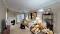This single-floor residence offers a thoughtfully designed layout that seamlessly connects the main living areas. The open-concept living and dining space serves as the heart of the home, featuring crown molding, neutral warm-toned walls, and soft carpeting throughout. The living area is anchored by a classic fireplace and benefits from natural light streaming through large windows with blinds and access to an outdoor area via a glass door, complemented by a ceiling fan overhead. Framed artwork and tasteful décor lend a welcoming ambiance.

The dining area flows directly from the living space and is enhanced by a mirrored accent wall that amplifies the sense of openness, alongside an overhead flush-mount light fixture.

The kitchen is a functional galley-style space outfitted with rich dark wood cabinetry, white appliances including a stove, refrigerator, and built-in microwave, and clean white tile flooring. An in-unit washer and dryer are conveniently located just off the kitchen.

The bedroom is generously sized with plush carpet, crown molding, a ceiling fan, large windows offering outdoor views, and direct access to a walk-in closet. The bathroom presents a clean, bright aesthetic with white tile flooring, white cabinetry, a large vanity mirror, and ample counter space.