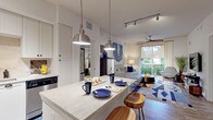 This single-floor residence offers a cohesive, well-designed interior with a consistent aesthetic throughout. The kitchen serves as a central highlight, featuring white beadboard cabinetry extending to the ceiling, stone-topped counters, a full suite of stainless steel appliances, tile backsplash, and a central island with seating for casual dining. Pendant lights and a track lighting system provide layered illumination over the workspace.

The living area is bright and comfortable, benefiting from a large sliding glass door that frames lush tropical greenery and opens to a private patio. A ceiling fan enhances airflow, while the verdant outdoor courtyard — filled with tall palms and dense landscaping — provides a serene natural backdrop.

The bedroom is a calm retreat with carpeted flooring, a ceiling fan, and a window overlooking greenery, offering a restful atmosphere. Two bathrooms echo the kitchen's design language, each featuring white beadboard vanities, stone countertops, large framed mirrors, and wood-look flooring. One bathroom includes a tub-shower combo with glass doors, while the other is appointed with a walk-in shower.

Throughout, wood-look and tile flooring, neutral walls, and consistent finishes create a polished, unified living environment.