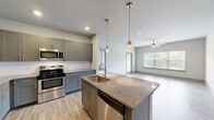 This well-appointed 2-bedroom, 2-bathroom residence at 100 Still Creek Ln in Athens, GA offers a thoughtfully designed single-floor layout with modern finishes throughout. The open-concept kitchen and living area serves as the heart of the home, featuring a central island with granite countertops, a stainless steel sink, and pendant lighting overhead. Gray shaker-style cabinetry pairs with a full suite of stainless steel appliances, including a refrigerator, range, microwave, and dishwasher, all set atop light wood-look flooring. The living area extends naturally from the kitchen, complete with a ceiling fan and a door leading to an outdoor balcony, filling the space with natural light. The spacious primary bedroom features plush carpeting, a ceiling fan, and multiple windows with outdoor views, alongside a private en-suite bathroom. The primary bath includes a granite-topped vanity with gray cabinetry, a soaking tub, separate shower, and access to a generous walk-in closet with wire shelving. The second bedroom is equally well-lit with dual windows and soft carpeting. The second bathroom mirrors the home's refined aesthetic with granite counters, blue-toned cabinetry, and a tub-shower combo.