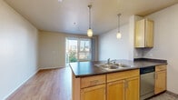 Located at 699 14th Street in San Diego's vibrant East Village neighborhood, this efficiently designed single-floor unit makes the most of its compact footprint. The open-concept kitchen and living area form the heart of the space, anchored by a peninsula with a dark countertop, double stainless steel sink, and warm natural wood cabinetry. Two pendant lights hang above the peninsula, adding a modern touch, while stainless steel appliances — including a refrigerator, range, and microwave — complete the kitchen. Light hardwood flooring runs throughout the living area, lending warmth and visual continuity. A sliding glass door floods the living space with natural light and opens onto a private balcony, offering open views of the surrounding San Diego cityscape. The hallway connects the main living area to the full bathroom, which features a wide vanity with dark countertops and natural wood cabinetry, a large wall mirror, tile flooring, and a shower-tub combination with additional overhead cabinet storage. The clean, neutral color palette throughout the unit creates a bright and cohesive ambiance well-suited to urban living in the heart of San Diego.