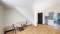 Located at 221 E State St in West Lafayette, Indiana, this two-story, 2-bedroom, 3-bathroom unit offers a functional and modern layout across two floors. The main level is the larger of the two and features a combined kitchen and living room area with light hardwood flooring, crisp white walls, and bold black accent doors that lend a contemporary contrast throughout. The kitchen is appointed with stainless steel appliances and tiled backsplash, while the adjacent dining area benefits from a distinctive angled ceiling, adding architectural character to the space. A hallway connects the main living areas to the bedrooms, each of which features hardwood floors, natural light from windows with blinds, and built-in desk and storage units suited for study or work. The bathrooms are cleanly finished with white subway tile surrounds in the tub and shower areas. The upper floor hosts a loft space finished with neutral carpet, providing a versatile secondary living or study area. With three full bathrooms distributed across the unit, the layout accommodates shared living with ease. The overall aesthetic is clean, minimalist, and functional, with consistent modern finishes throughout both levels.