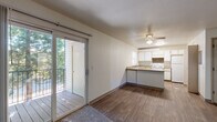 This single-floor, 3-bedroom, 1-bathroom unit offers an efficient and practical layout designed to maximize livability. The open-plan living and kitchen area forms the heart of the home, where wood-style hard flooring flows seamlessly underfoot. The kitchen features a peninsula counter that doubles as a breakfast bar, white cabinetry, a built-in range, and a full-size refrigerator, with a window providing natural light over the sink. A ceiling fan overhead keeps the living area comfortable year-round. Sliding glass doors lead from the living room to a private outdoor balcony, which overlooks a lush canopy of mature evergreen trees, creating a tranquil, nature-connected retreat. The three bedrooms are carpeted and bright, each with windows that invite natural light and views of the surrounding greenery, along with baseboard heating for added comfort. The shared bathroom is clean and functional, featuring a full tub-shower combination, a toilet, and a vanity with countertop. Neutral wall tones and textured ceilings carry throughout the unit, lending a consistent and understated aesthetic. The space is thoughtfully arranged to accommodate a variety of living needs within a cozy and manageable footprint.