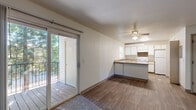 This single-floor, 3-bedroom, 1-bathroom unit offers an efficient and practical layout designed to maximize livability. The open-plan living and kitchen area forms the heart of the home, where wood-style hard flooring flows seamlessly underfoot. The kitchen features a peninsula counter that doubles as a breakfast bar, white cabinetry, a built-in range, and a full-size refrigerator, with a window providing natural light over the sink. A ceiling fan overhead keeps the living area comfortable year-round. Sliding glass doors lead from the living room to a private outdoor balcony, which overlooks a lush canopy of mature evergreen trees, creating a tranquil, nature-connected retreat. The three bedrooms are carpeted and bright, each with windows that invite natural light and views of the surrounding greenery, along with baseboard heating for added comfort. The shared bathroom is clean and functional, featuring a full tub-shower combination, a toilet, and a vanity with countertop. Neutral wall tones and textured ceilings carry throughout the unit, lending a consistent and understated aesthetic. The space is thoughtfully arranged to accommodate a variety of living needs within a cozy and manageable footprint.