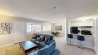 Located at 8 Lakeview Gardens in Natick, Massachusetts, this single-floor residence offers a well-designed, open-concept layout that maximizes both comfort and functionality. The living area is generously proportioned, featuring plush carpeting, neutral walls, and large windows that allow natural light to fill the space. A dedicated seating area with ample room for relaxed gathering flows seamlessly into the dining area, which features a glass-top round table with modern chairs positioned beneath a window overlooking the outdoors.

The kitchen is thoughtfully designed with white cabinetry, granite countertops, and black appliances including a refrigerator and range. A peninsula counter with bar seating connects the kitchen to the main living space, enhancing the open feel and providing additional dining options.

The residence includes two carpeted bedrooms, each offering a quiet retreat with natural light, closet storage, and a calm, neutral color palette. The bathroom is clean and functional, complete with a full tub and shower combination.

Throughout the home, a cohesive design aesthetic is maintained with warm neutral tones, soft carpeting, and tasteful décor. The space offers a comfortable and practical living environment in a well-established Natick community.