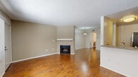 Located at 6210 Woodman Ave in Los Angeles, this one-bedroom, one-bathroom unit offers a well-organized single-level layout. Rich hardwood flooring runs throughout the main living areas, anchoring the open-concept living and dining space. A standout feature of the living room is the tile-surround fireplace with a white mantel, adding a classic, functional focal point to the room. The space flows naturally toward the kitchen, which is accessible via an open pass-through and features light wood cabinetry, granite-style countertops, and stainless steel appliances including a gas range and refrigerator. A pendant light fixture illuminates the dining area just off the kitchen. The bedroom is carpeted for comfort and offers a generous sliding-door closet along with a large window that frames views of the surrounding neighborhood greenery, allowing ample natural light to fill the room. The full bathroom includes a wood-toned vanity with a single sink, a large mirror, and a shower-tub combination with a frosted glass enclosure. A textured ceiling is consistent throughout the unit. The layout is efficient and practical, making smart use of the available space for comfortable everyday living in the Van Nuys neighborhood of Los Angeles.