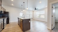 This single-story space is designed with a clean, contemporary aesthetic that emphasizes an open and functional layout. The kitchen serves as a central hub, anchored by a substantial island with a granite countertop and an undermount sink with a pull-down faucet. Three pendant lights hang above the island, providing focused task lighting. Dark espresso cabinetry lines the kitchen walls, paired with granite countertops and a full suite of stainless steel appliances, including a range, over-the-range microwave, and refrigerator. Open shelving adds a modern touch alongside the upper cabinets.

Light wood-style flooring runs consistently throughout the unit, creating a cohesive and airy feel. The living area extends naturally from the kitchen and is brightened by multiple windows dressed with horizontal blinds, allowing ample natural light. A ceiling fan overhead enhances comfort in this shared living space.

The bedrooms are well-proportioned, each featuring a ceiling fan, large windows with exterior views, and access to walk-in closet space. Two bathrooms serve the unit—one with a tub-shower combination and dark vanity cabinetry, and another with a glass-door walk-in shower, matching granite vanity top, and wood-tone tile flooring. The overall ambiance is modern, neutral, and move-in ready.