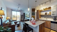 This single-story residence is thoughtfully designed with an open-concept layout that seamlessly connects the living, dining, and kitchen areas. The living room is anchored by a leather sectional sofa, ceiling fan, and large sliding glass doors that open onto a private balcony with outdoor views of mature trees and greenery, filling the space with natural light.

The kitchen is well-equipped with warm wood cabinetry, stainless steel appliances including a refrigerator, range, and microwave, a striped tile backsplash, hardwood-style flooring, and a peninsula island with pendant lighting that doubles as a casual dining area.

The space includes two bedrooms, each featuring ceiling fans and ample natural light. One bedroom offers a walk-in closet, while the other provides generous shelving and storage. Two bathrooms serve the unit—one with a tiled shower-tub combination and clean white finishes, and another with a glass-enclosed walk-in shower and a bold decorative wall treatment.

A dedicated in-unit laundry area houses a full-size washer and dryer with built-in shelving overhead. Hardwood-style flooring flows throughout the main living areas, contributing to the cohesive and modern ambiance of the residence.