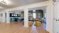 Located at 5816 Westpark Drive in Charlotte, NC, this single-floor space offers a thoughtfully designed open-concept layout that seamlessly connects a well-appointed kitchen and a generous living area. Warm hardwood-style flooring flows throughout, complemented by crisp white structural columns that define zones while preserving an airy, connected feel. Crown molding and sputnik-style light fixtures add refined architectural details to the ceilings.

The living area is anchored by vaulted, angled ceilings that lend impressive vertical scale and drama. Sage green accent walls provide a rich, contemporary backdrop, while oversized black-framed windows invite abundant natural light and offer views of lush outdoor greenery. An entry zone features tufted yellow ottomans and open sightlines through glass-paneled doors, creating a welcoming first impression.

The kitchen stands out with its retro-modern mint green cabinetry, sleek white countertops, and a striking dark subway tile backsplash. A central island with bar seating encourages casual gathering, while pendant lighting adds a bold finishing touch. The overall ambiance is modern and vibrant, balancing bold design choices with a comfortable, functional layout well-suited for social interaction and community use.