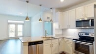 Located at 4450 Tropea Way in Jacksonville, Florida, this single-floor residence offers a clean, contemporary design with a bright and airy atmosphere throughout. The open-concept kitchen is a standout feature, outfitted with white shaker-style cabinetry, granite countertops, a classic subway tile backsplash, and a full suite of stainless steel appliances including a refrigerator, range, microwave, and dishwasher. Pendant lighting over the kitchen peninsula adds a stylish touch, while the layout flows naturally into the living area. The living space features wood-style plank flooring, a ceiling fan, and French doors that open onto a private balcony, allowing for an abundance of natural light and outdoor views. Bedrooms are finished with plush carpeting, ceiling fans, and windows that bring in natural light. The primary bedroom connects to a well-appointed bathroom featuring a granite-topped vanity with white cabinetry, a large framed mirror, and a tiled shower. A spacious walk-in closet with wire shelving provides generous storage. Additional rooms offer wood-style flooring and clean white walls, providing versatile living spaces. The overall ambiance is modern, light-filled, and move-in ready.