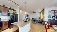 This single-floor residence offers a thoughtfully designed open-concept layout that seamlessly connects the kitchen, dining, and living areas. The kitchen is a standout feature, showcasing rich dark wood cabinetry, granite countertops, a granite-topped island with pendant lighting, tile flooring, and black appliances including a French door refrigerator, range, microwave, and dishwasher. Track lighting overhead adds a modern touch. The living room is generously sized with plush carpeting, a ceiling fan, and large windows dressed with patterned drapes that flood the space with natural light and offer views of surrounding greenery. Two well-sized bedrooms each feature carpeted floors, ceiling fans, and bright windows. The primary bedroom includes an arched niche detail and ample space for a dresser and seating. The two bathrooms are finished with tile flooring and dark wood vanities with granite countertops. The primary bathroom features a soaking tub set within an arched alcove, while the secondary bathroom offers a glass-enclosed walk-in shower. Throughout the residence, a warm, neutral color palette and consistent finishes create a cohesive and comfortable living environment.