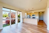 Located at 2731 Rucker Ave in Everett, WA, this well-appointed 2-bedroom, 2-bathroom residence offers a thoughtfully designed single-level layout. The open-concept living, dining, and kitchen area serves as the heart of the home, bathed in natural light from expansive floor-to-ceiling sliding glass doors that frame beautiful views of lush, colorful landscaping. The kitchen features light wood cabinetry, stainless steel appliances including a refrigerator, microwave, and range, a central island with a built-in sink, and stylish pendant lighting overhead. Light-toned hardwood flooring flows seamlessly throughout the entire unit, lending a clean and cohesive aesthetic. Both bedrooms are generously proportioned, each with large sliding glass doors that open to striking views of the surrounding neighborhood and the water beyond. The two bathrooms are clean and functional, featuring light wood vanities with stone-topped counters, large mirrors, and tiled tub-shower combinations. A dedicated hallway connects the living spaces to the private quarters, with a closet providing additional storage. The overall ambiance is bright, modern, and airy, ideal for comfortable everyday living in a prime Everett location.