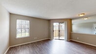 This single-floor unit offers a thoughtfully designed layout that balances comfort and functionality. The main living area is bright and open, featuring durable hardwood-style flooring, neutral warm-toned walls, and a textured ceiling. A sliding glass door fills the space with natural light and provides direct access to a private balcony with outdoor views, while a side window further enhances the airy feel. A pass-through opening connects the living area to the kitchen, which is well-equipped with dark wood cabinetry, light quartz-style countertops, black appliances including a range and over-the-range microwave, and a stylish tile mosaic backsplash that adds a modern touch. The bedroom is a comfortable retreat with plush carpeting, a ceiling fan with integrated lighting, and a window that invites natural light. A dedicated in-unit laundry closet provides added convenience, housing a full-sized washer and dryer with overhead shelving. The bathroom is clean and functional, featuring hardwood-style flooring, a bathtub, and brushed nickel fixtures. Throughout, the consistent neutral color palette and clean finishes create a cohesive and inviting atmosphere.