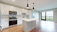 This single-floor residence showcases a contemporary design with a cohesive neutral palette, light wood-look flooring, and soft carpeting in the bedrooms. The open-concept kitchen serves as the heart of the unit, featuring white shaker cabinetry with matte black hardware, a subway tile backsplash, quartz countertops, and a central island with pendant lighting overhead. A full suite of stainless steel appliances—including a gas range, refrigerator, built-in microwave, and dishwasher—completes the space.

The living area flows naturally from the kitchen and benefits from expansive floor-to-ceiling windows that frame sweeping panoramic views of the surrounding landscape, filling the space with abundant natural light. Bedrooms are finished with plush carpeting and offer generous closet space, including a walk-in closet with wire shelving systems. One bedroom captures particularly impressive elevated views through its large corner window.

Two bathrooms serve the unit: one features a glass-enclosed walk-in shower with vertical subway tile and a white vanity with matte black fixtures, while the second offers a combined tub-shower with dark hardware accents. A dedicated in-unit laundry room houses a full-size Whirlpool washer and dryer with additional wire shelving for storage.