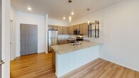 Located at 7805 S Dakota Hawk Ave in Sioux Falls, South Dakota, this single-floor residence offers a clean, modern design with a thoughtful layout and quality finishes throughout. Light wood-style flooring flows through the main living areas, creating a warm and cohesive aesthetic that complements the bright, neutral palette of the walls and trim.

The kitchen serves as a central highlight of the space, featuring a large granite-topped island with an integrated sink, taupe shaker-style cabinetry, stainless steel appliances, and stylish pendant lighting overhead. Open shelving with a metal frame adds a contemporary touch and connects seamlessly to the main living area.

The living area is generously sized and filled with natural light, anchored by a full-width sliding glass door fitted with vertical blinds that opens to a private balcony with views of the surrounding area. A separate bedroom features soft wall-to-wall carpeting and a window with horizontal blinds, offering a quiet and comfortable retreat.

The bathroom is well-appointed with the same light wood flooring, a granite-topped vanity with warm cabinetry, and a full tub-shower combination with a curved curtain rod. Recessed lighting throughout the unit adds a polished finish, while the overall layout prioritizes both functionality and comfort in a contemporary residential setting.
