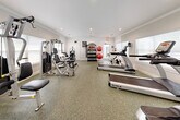 The Avana Acworth Fitness Center is a comprehensively outfitted single-floor exercise facility designed to support a wide range of workout routines. The space features a clean, neutral aesthetic with white walls accented by crown molding, recessed lighting, and durable speckled rubber flooring suited for high-traffic athletic use. Large windows line the perimeter, allowing natural light to fill the room and creating an open, airy atmosphere.

The cardio zone is stocked with True-brand treadmills, an elliptical, and a stationary spin bike, providing ample options for aerobic training. A wall-mounted flat-screen television is positioned nearby for entertainment during workouts. The strength training area includes multiple multi-function cable and weight machines, a leg press, and dedicated benches for targeted resistance exercises. A full-length wall mirror spans one side of the room, visually expanding the space and allowing users to monitor their form.

A centrally located free weight station features a well-organized rack holding a complete set of dumbbells, kettlebells, medicine balls, and stability balls, catering to functional and dynamic training needs. Informational signage and fitness center rules are clearly posted near the entrance. The facility offers a bright, well-maintained environment appropriate for both casual and serious fitness routines.