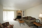 This single-floor residence offers a comfortable and functional layout across several well-defined living spaces. The living room serves as the heart of the home, anchored by a striking full brick fireplace with a raised hearth and built-in shelving alongside it, creating a warm and inviting focal point. Soft carpeting and a textured ceiling carry throughout the common areas and bedrooms, lending a consistent, cozy feel.

Adjacent to the living room, the dining area features a ceiling fan, vertical blinds covering a sliding door that allows natural light to filter in, and ample space for a dining set. The kitchen is equipped with dark cabinetry, light countertops, a gas range, dishwasher, and a full-size refrigerator, all set on easy-care tile flooring.

The bedrooms are generously sized, each with plush carpet and windows fitted with blinds. The primary bedroom includes a walk-in closet, adding valuable storage. Additional rooms provide flexible space that can serve as bedrooms or other purposes.

The bathroom features an extended vanity with a granite-style countertop, dark wood cabinetry, a wide wall mirror with overhead lighting, and a tiled shower-tub combination with chrome fixtures. Throughout, neutral tones and practical finishes create a clean, move-in ready environment.