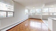 This 2-bedroom, 1-bathroom unit offers a practical and comfortable layout across a single floor. The combined kitchen and living area serves as the heart of the home, with the living room showcasing warm, polished parquet hardwood flooring in a classic herringbone pattern and large windows that invite generous natural light and outdoor views. Baseboard heating runs along the perimeter of each room, ensuring even warmth throughout.

The kitchen is well-equipped with white shaker-style cabinetry, dark countertops, a stylish tile backsplash, and a full suite of stainless steel appliances including a refrigerator, electric range, microwave, and dishwasher. White ceramic tile flooring and a bright window overlooking greenery complete the kitchen's clean, functional aesthetic.

Both bedrooms continue the parquet hardwood flooring and feature large windows with views of the surrounding building landscape. The primary bedroom includes a mirrored sliding-door closet, maximizing both storage and the sense of space. The second bedroom is equally well-lit and versatile.

The bathroom features neutral large-format wall tiles, a soaking tub with shower, a window for natural ventilation, and a mirrored vanity. Two hallways connect the rooms efficiently. Overall, the unit presents a bright, cohesive, and move-in-ready living space.