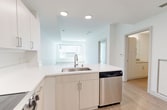 This 670-square-foot, one-bedroom, one-bathroom apartment is located at 317 112th Avenue NE in Bellevue, WA. The unit features a clean, modern design throughout, with light-toned hardwood-style flooring and crisp white walls that create a bright, airy atmosphere across all rooms.

The open-concept kitchen and living area serves as the heart of the unit. The kitchen is well-appointed with white flat-front cabinetry, quartz countertops, a peninsula with an integrated sink, and a full suite of stainless steel appliances including a refrigerator with water dispenser, electric range, over-the-range microwave, and dishwasher. Recessed lighting illuminates the kitchen efficiently.

The living room is spacious and filled with natural light, courtesy of large floor-to-ceiling windows that provide views of the surrounding Bellevue streetscape. The open layout allows for flexible furniture arrangements.

The primary bedroom measures 140 square feet and includes a window that brings in ample natural light. A dedicated closet provides convenient storage. The bathroom features light wood-toned cabinetry, a single vanity with sink, a toilet, and a bathtub/shower combination, all finished in a clean, neutral palette. The unit also includes a dedicated closet for additional storage needs.