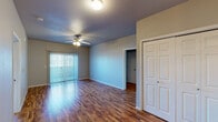 This single-floor residence offers a thoughtfully designed layout that balances comfort and functionality throughout. The living area is highlighted by rich hardwood flooring, a ceiling fan with light fixture, and a sliding vertical-blind window treatment that allows natural light to fill the room. A double-door closet adds convenient storage directly off the main living space. The dining area transitions seamlessly from the living room, featuring tile flooring and pendant lighting overhead, creating a natural flow into the kitchen. The kitchen is well-equipped with warm oak cabinetry, granite-style countertops, black appliances including an electric range and built-in microwave, and matching tile flooring. The residence includes multiple bedrooms, each carpeted and fitted with ceiling fans and windows with horizontal blinds that bring in natural light. Closet space is provided in the bedrooms, including a sliding-door closet. Two bathrooms serve the home, each featuring tile flooring, wood vanity cabinetry, and granite-style countertops. One bathroom includes a full tub-shower combination and a wall-mounted storage cabinet, while the second offers a bright window for added ventilation. Throughout the home, neutral gray wall tones create a clean, cohesive aesthetic.
