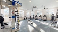 Located in Spring Hill, Tennessee, this fitness center offers a thoughtfully designed, single-floor layout divided into two distinct workout areas. The main exercise room is generously proportioned, featuring large multi-pane windows along multiple walls that flood the space with abundant natural light and provide views of the surrounding greenery. Ceiling fans keep the environment comfortable, while durable, tile-patterned flooring supports a comprehensive array of equipment including treadmills, ellipticals, rowing machines, a recumbent bike, a Smith machine, a cable crossover station, and an Octagon functional training rig complete with a full dumbbell rack and accessory storage. A weight bench and stability balls round out the strength and conditioning offerings. The second room serves as a dedicated cycling and yoga studio, featuring light wood-toned flooring, large windows with blinds, and high transom windows that maximize daylight. Two Peloton-style spin bikes and rolled yoga mats make it ideal for focused, low-impact workouts. Throughout both spaces, crisp white walls, recessed lighting, and modern ceiling fans contribute to a clean, bright, and welcoming atmosphere well-suited for a full range of fitness activities.