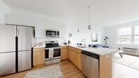 This single-floor residence showcases a thoughtfully designed contemporary interior with a cohesive aesthetic carried throughout. The open-concept kitchen is a standout feature, combining warm natural wood cabinetry on the lower levels with crisp white upper cabinets, all topped with light-toned countertops. A full suite of stainless steel appliances — including a French door refrigerator, electric range, over-the-range microwave, and dishwasher — provides comprehensive functionality. Pendant lighting above the peninsula adds a modern touch, and the layout flows seamlessly into the living area.

The living room benefits from a large window that draws in natural light and offers views of the surrounding neighborhood. Light hardwood flooring extends throughout the main living spaces, reinforcing the unit's clean, airy feel.

The bedroom is a calm, well-proportioned retreat with crisp white walls, hardwood floors, and notable storage provided by multiple closets, including a sliding-door closet and an additional storage room. The bathroom features dark tile flooring, a wood-toned vanity with a white countertop, and a full shower-tub combination, rounding out this well-appointed space.