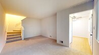 This two-floor townhouse offers a practical and comfortable layout across two bedrooms and one and a half bathrooms. The main level features a carpeted living area with neutral-toned walls, a front entry door, and windows that allow natural light to filter in. A staircase with a handrail connects the two floors, adding a classic townhouse feel to the interior flow. The kitchen is well-appointed with warm wood cabinetry, granite-style countertops, hardwood-style flooring, and includes a dishwasher. A dedicated laundry area just off the kitchen houses a stacked washer and dryer unit, adding everyday convenience. The half bathroom on the main level features wood vanity cabinetry, a granite-style countertop, a large mirror, and a window for natural light. Upstairs, both bedrooms are carpeted and generously sized. The primary bedroom includes a ceiling fan with light fixture and windows overlooking greenery outdoors. The second bedroom also features a window with outdoor views. The full bathroom upstairs mirrors the half bath's finishes, with wood cabinetry, a granite-style vanity top, tile flooring, and a window. Throughout, the townhouse maintains a consistent, neutral palette that offers a clean and move-in-ready atmosphere.