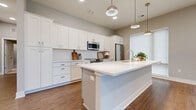 Located in Dublin, Ohio, this well-appointed 2-bedroom, 2-bathroom single-story home offers a thoughtfully designed layout with modern finishes throughout. The open-concept kitchen and living area serves as the heart of the home, showcasing white shaker cabinetry, a white quartz countertop island with pendant lighting, a subway tile backsplash, and stainless steel appliances including a built-in microwave and French door refrigerator. Warm wood-tone luxury vinyl flooring runs throughout the main living areas, complementing the neutral gray wall palette and clean white trim. A glass-panel door introduces natural light into the living space, creating an airy, connected feel. The spacious primary bedroom features plush carpet, mirrored sliding closet doors, and a dedicated walk-in closet with wire shelving. The en suite bathroom is finished with white shaker vanity cabinetry, quartz countertops, a frameless glass walk-in shower, and wood-look flooring. The second bathroom mirrors the same refined aesthetic with a full vanity and ample storage. A dedicated laundry room houses a full-size washer and dryer alongside the water heater and HVAC system. The second bedroom is generously sized with carpeted floors and a wall-length closet, offering flexible use as a guest room or home office.