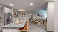 Located in Tomball, TX, this thoughtfully designed 2-bedroom, 2-bathroom single-story residence offers a comfortable and functional living experience. The open-concept main living area seamlessly connects the kitchen, dining, and living room, creating a bright and inviting atmosphere. The kitchen is a standout feature, boasting a large granite-topped island with bar seating, stainless steel appliances including a refrigerator, range, and microwave, and contemporary light-wood cabinetry with recessed lighting throughout. Adjacent to the kitchen, the dining area provides an intimate space accented by stylish wall shelving. The living room offers wood-style plank flooring, a ceiling fan, and natural light through large windows with blinds and access to an exterior door. Both bedrooms are carpeted and equipped with ceiling fans, ample natural light, and walk-in closets with wire shelving systems. The primary bedroom features a spacious walk-in closet and a private en-suite bathroom with granite vanity countertops and wood-toned cabinetry. The second bathroom mirrors the same refined finishes. A dedicated laundry room houses a full-size washer and dryer with overhead shelving, adding everyday convenience to this well-rounded home.