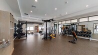 Located at 2300 Reservoir Ave in Trumbull, CT, this single-story fitness center offers a comprehensive, multi-zone workout facility designed to accommodate a wide range of exercise needs. The space is thoughtfully organized into distinct areas, each serving a specific fitness function.

The main strength training area is expansive and bright, featuring recessed lighting and high ceilings that contribute to an open, energizing atmosphere. It is outfitted with a cable machine, power rack, weight benches, a heavy bag, a ceiling-mounted functional training rig with suspension equipment, and plyo boxes, all set on durable rubber flooring. Large mirrors line the walls, enhancing the sense of space. Black-framed glass partitions divide zones while maintaining visual connectivity throughout.

A dedicated cardio section houses multiple treadmills and stair climbers positioned beneath a row of windows, allowing natural light and outdoor views. A separate cycling and rowing studio, finished in deep gray tones, accommodates spin bikes and a rowing machine, with windows framing exterior views.

An additional studio space features warm hardwood flooring, a frosted glass panel door, and natural light, providing an ideal setting for yoga or group fitness. A water station and built-in storage unit serve the entry area, completing this well-appointed facility.