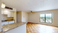 Located at 925 California Ave in Avalon, PA, this single-floor unit offers a practical and efficiently designed layout across a cozy footprint. The combined kitchen and living area forms the heart of the space, anchored by distinctive parquet wood flooring that runs throughout. The kitchen is outfitted with white cabinetry, granite countertops, a white electric range, a stainless steel sink, and a built-in microwave above the stove. A peninsula with a matching granite surface provides additional prep space and defines the transition between the kitchen and the open living area. The living room is bright and airy, benefiting from a large window that frames neighborhood views and allows natural light to fill the room. A ceiling fan overhead adds both function and a finishing touch. Neutral, warm-toned walls complement the natural wood tones of the parquet flooring throughout. The bathroom features a full tub and shower combo with white tile surround, accessibility grab bars, a white vanity with storage, and tile flooring. The entry door opens directly into the main living space, contributing to the unit's efficient and straightforward flow. Overall, the space offers a clean, functional, and comfortable environment.