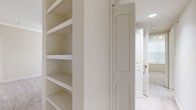 This single-story residence is thoughtfully designed to maximize functionality and comfort across its well-proportioned layout. The open-concept living area serves as the heart of the home, featuring plush wall-to-wall carpeting, crown molding, and a ceiling fan. Track lighting accentuates the transition between the living space and kitchen, while a half-wall peninsula defines the boundary between the two areas.

The galley-style kitchen is appointed with rich, dark cherry cabinetry, granite-toned countertops, and tile flooring. Black appliances, including a range, microwave, and refrigerator, complement the cabinetry. A built-in shelving nook adjacent to the kitchen provides additional storage or display space.

The bedrooms are carpeted and receive natural light through blinds-fitted windows. One bedroom connects to a bathroom featuring cherry vanity cabinetry, granite-style countertops, a tub-shower combination, and tile flooring, with the added convenience of an adjoining closet with wire shelving.

A second full bathroom mirrors the design aesthetic, with matching cabinetry and a tub-shower combination. Additional built-in shelving units in the hallway area offer versatile storage solutions, completing the practical and cohesive character of this residence.