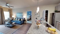 This single-floor, 2-bedroom, 2-bathroom residence offers a well-designed open-concept layout that seamlessly connects the kitchen, dining, and living areas. The kitchen is appointed with granite countertops, a stainless steel sink, and elegant pendant lighting that hangs above the island, creating a functional yet stylish centerpiece for the space. The flooring throughout the main living area features wood-style planks that add warmth and continuity.

The living area is generously proportioned, providing ample room for comfortable furnishings. Neutral wall tones complement the space's coastal-inspired aesthetic, allowing for versatile decorating possibilities. A visible bedroom off the main living area showcases carpeted flooring and a thoughtful layout, offering a private retreat within the residence.

The open sightlines throughout the main living spaces enhance the sense of flow and connectivity. Recessed ventilation, modern lighting fixtures, and clean architectural lines contribute to a polished, contemporary feel. The overall ambiance is bright and welcoming, making this residence a comfortable and functional living environment suited for everyday living.