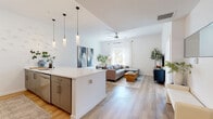 Located in the heart of Phoenix's vibrant Roosevelt Row Arts District at 301 W Roosevelt St, this well-appointed one-bedroom, one-bathroom residence offers a thoughtfully designed open-concept floor plan on a single level. Light wood-look flooring flows throughout, complementing the crisp white walls and creating a bright, cohesive aesthetic.

The combined living, dining, and kitchen area forms the heart of the home. The kitchen is equipped with stainless steel appliances including a French door refrigerator, electric range, and microwave, all framed by white shaker cabinetry and a large white quartz waterfall island with seating for multiple bar stools. Elegant cylindrical pendant lights hang above the island, adding a modern touch. The open living area receives generous natural light through large windows dressed in sheer white curtains, and a ceiling fan keeps the space comfortable.

The bedroom offers a serene retreat with a bright window framing outdoor greenery and city views, along with a dedicated closet. The full bathroom impresses with dual vanity sinks, white cabinetry, and a floor-to-ceiling marble-tiled walk-in glass shower. In-unit laundry adds everyday convenience, completing this polished urban residence.