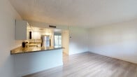 Located at 7633 NW 42nd Pl in Sunrise, Florida, this single-story space presents a clean, move-in-ready interior with a cohesive design aesthetic carried throughout. Light wood-style flooring runs continuously across the main living areas and bedrooms, lending a bright, airy quality to the space and complementing the crisp white walls and textured ceilings found in every room.

The open-concept living area connects seamlessly to the kitchen via a peninsula counter finished with granite surfaces, offering a natural gathering point while maintaining an open sight line. The kitchen is well-appointed with white raised-panel cabinetry, granite countertops, stainless steel appliances including a range, microwave, dishwasher, and refrigerator, as well as recessed lighting overhead. A sliding glass door in the kitchen area allows natural light to filter into the living space and provides views of the surrounding greenery.

The additional rooms feature the same neutral palette with wood-style flooring, offering versatile use as bedrooms or living spaces. The bathroom is finished with a granite-topped vanity with white cabinetry, tile surround on the tub/shower, and light wood flooring, maintaining a consistent, updated look throughout the entire space.