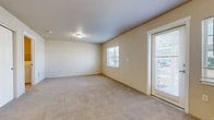 Located at 12928 E Mansfield Ave in Spokane Valley, WA, this single-floor unit offers a practical and efficiently laid-out living space. The open-concept design seamlessly connects the kitchen and living room, maximizing functionality within a cozy footprint.

The kitchen is well-appointed with warm wood cabinetry, light countertops, and a full suite of black appliances including a refrigerator, range, built-in microwave, and dishwasher. A peninsula-style breakfast bar separates the kitchen from the living area, providing additional prep and dining space. Pendant lighting above the bar adds a functional accent, while tile flooring throughout the kitchen ensures easy maintenance.

The living area features neutral-toned carpet, soft beige walls, and multiple windows that allow natural light to filter in throughout the day. A glass exterior door provides direct outdoor access and further brightens the space. A wall-mounted air conditioning unit ensures year-round comfort.

A separate carpeted room, visible in the floor plan, offers closet storage and an adjoining utility area, adding to the unit's overall practicality. The clean, neutral palette throughout creates a versatile backdrop suitable for a variety of interior styles. Overall, the unit presents a straightforward, functional layout well-suited to everyday living.