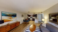 This thoughtfully designed single-floor residence blends mid-century modern aesthetics with contemporary finishes throughout its open, flowing layout. The living area is anchored by warm hardwood-style flooring, large windows that invite natural light, and a built-in desk nook accented by a bold amber feature wall — an ideal dedicated workspace integrated seamlessly into the living space. The open-concept plan connects the living area to the dining space and kitchen, creating a cohesive environment well-suited for both relaxing and entertaining. The kitchen is well-appointed with rich dark cabinetry, stone-look countertops, a decorative tile backsplash, stainless steel appliances, and a skylight that adds additional brightness to the space. The bedroom offers a serene retreat, highlighted by a soft teal accent wall, textured ceiling, and ample closet storage. The bathroom features a combination tub and shower, dark vanity cabinetry with a clean white countertop, and wood-style tile flooring that ties back to the rest of the home. Neutral wall tones, textured ceilings, and cohesive flooring throughout provide a versatile canvas that complements the space's distinct mid-century modern character.
