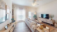 Located at 25335 Budde Rd in Spring, TX, this single-floor residence offers a thoughtfully designed layout with a warm, cohesive aesthetic throughout. Wood-look plank flooring runs through the main living areas, complementing the neutral, light-toned walls that create a bright and welcoming atmosphere.

The living room is a comfortable centerpiece of the home, featuring a ceiling fan with light fixture, large windows dressed with sheer white curtains that invite abundant natural light, and direct access to an exterior door. Adjacent to the living space, the dining area provides a defined space for meals, accented by crown molding, decorative wall art, and natural light from nearby windows.

The kitchen is equipped with a coil-burner range, ample wood-toned cabinetry, and neutral countertops, opening conveniently toward the dining area. The bedrooms are generously proportioned, each with ceiling fans, large windows, and wood-look flooring. The primary bedroom includes access to a walk-in closet with wire shelving for organized storage.

The bathroom features a tub-shower combination, a single-sink vanity with substantial counter space, and wood-look flooring. A dedicated laundry area with a washer and an electrical panel rounds out the practical amenities of this well-equipped home.